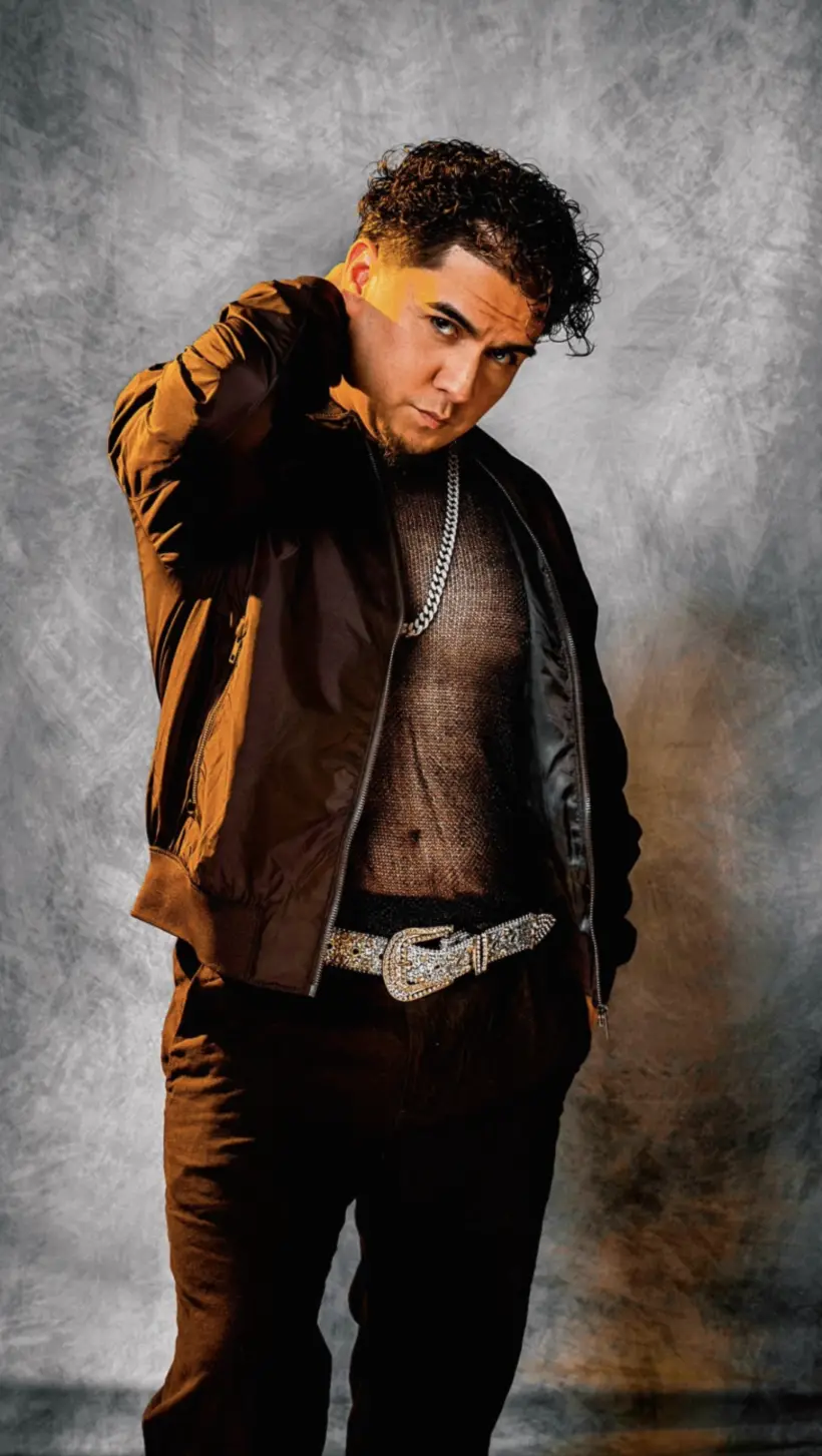 Raél in black, lit by warm amber light against a gray studio backdrop